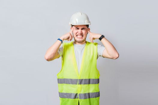 Young engineer covering his ears isolated, Builder man with ear pain, Concept of engineer covering his ears with pain expression, Engineer with ear pain isolated