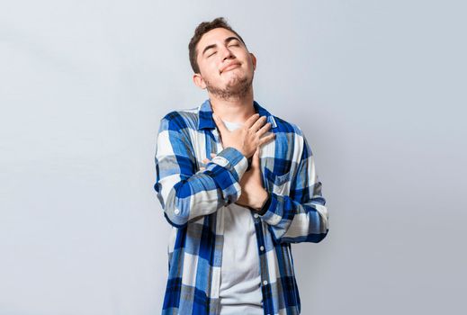 Grateful young guy smiling with hands on chest, isolated. Positive young man with charming sincere smile feeling grateful. relaxed person with gesture of thanks with hands on chest