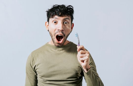 Surprised young man holding a toothbrush. Amazed teenager holding toothbrush isolated, Guy holding toothbrush with amazed face isolated on white