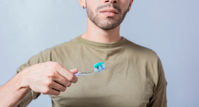 Guy with unrecognizable face holds brush with toothpaste on isolated background, shows toothbrush
