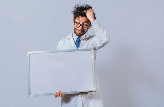 Male scientist in white coat holding and pointing at a blank whiteboard. Disheveled-haired man holding blank whiteboard, Amazed man in white coat pointing at a whiteboard