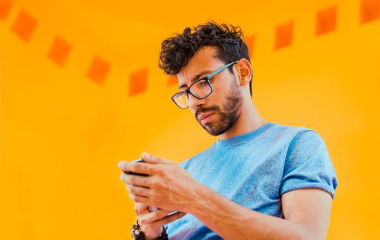 Lifestyle of handsome bearded man using cell phone outdoors. Low angle view of young man using cell phone outdoors. Guy sending a message with a cell phone near a yellow wall outdoors