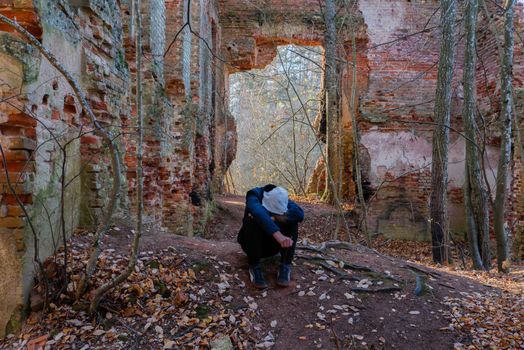 The boy dropped his head to his knees. A teenager sits in an abandoned building. Depressed Teenager man sitting alone on Wall in Outdoor.Unpleasant pain. High quality photo