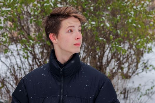 Portrait of a cute positive boy 15-17 years old in a black jacket in winter. Portrait of a boy in profile.