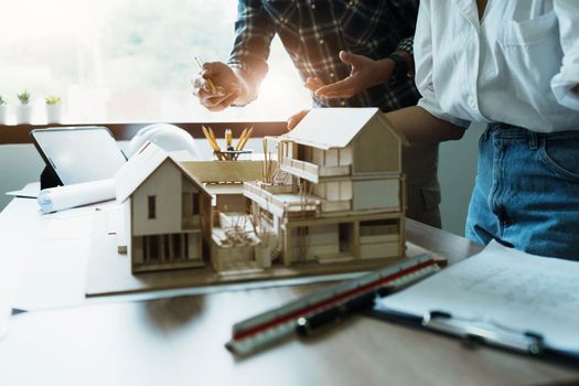 Engineers are consulting the team to design an architectural structure for clients with blueprints and building models to work at office.