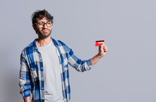 Person holding and looking at credit card with distrust, Confused handsome man holding credit card isolated. Insecure young man holding a credit card. Concept distrust with credit cards