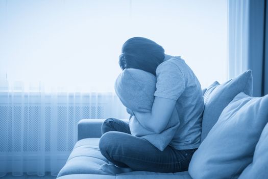 Sad depressed woman at home, she is sitting on the couch and hugging a pillow, loneliness and sadness concept