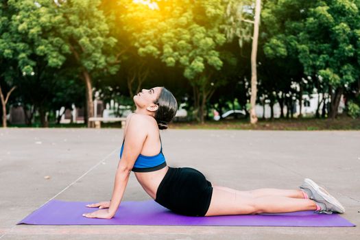 Sporty woman stretching her body doing cobra pose in a park. Athlete woman doing cobra pose in a park. Athlete woman doing yoga Bhujangasana in a park