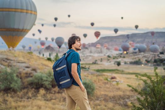 Tourist man looking at hot air balloons in Cappadocia, Turkey. Happy Travel in Turkey concept. Man on a mountain top enjoying wonderful view.