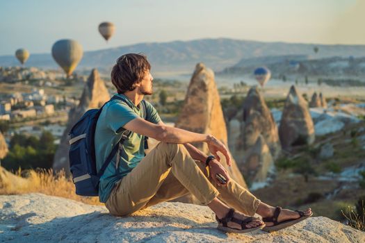 Tourist man looking at hot air balloons in Cappadocia, Turkey. Happy Travel in Turkey concept. Man on a mountain top enjoying wonderful view.