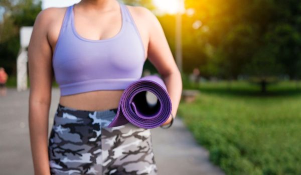 Unrecognizable woman holding a mat in the park. Athlete woman's hands carrying the mat after exercising. Fitness woman concept carrying yoga mat with copy space