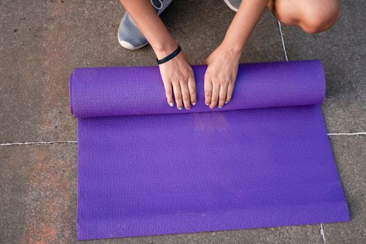 Woman hands rolling up the mat outside. Athlete woman's hands rolling up the mat after exercising. Concept of rolling up mat after exercise