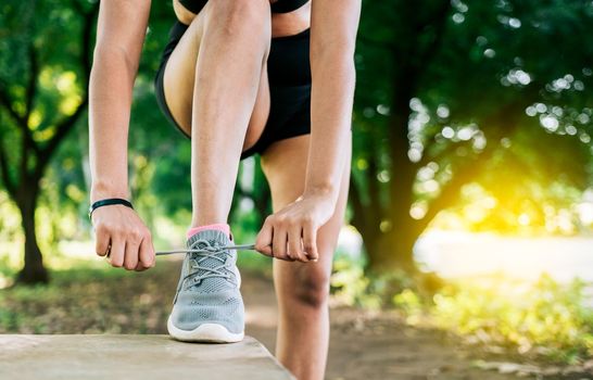 Close-up of sporty woman tying her shoes. Athletic girl tying her shoe laces in a park. Runner girl tying her running shoes in a park with copy space