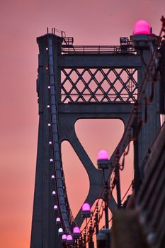 Image of Pink lights in detail on support wires of American bridge with golden light behind