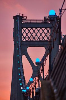 Image of Blue lights in detail on support wires of American bridge with golden light behind