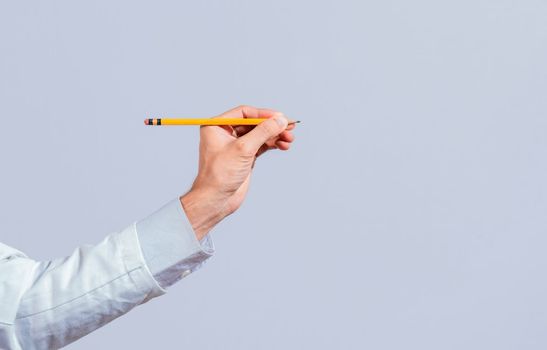 Male hand holding a pencil on a blank. Man fingers holding a pencil with blank space. Person hands holding a pencil on a space for text, Hand with a pencil pointing at a blank space