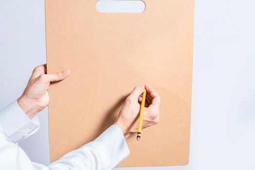 Close up of doctor hands with pencil over clipboard with copy space. Doctor hands writing on blank wooden clipboard isolated. Concept of hands writing on blank wooden clipboard