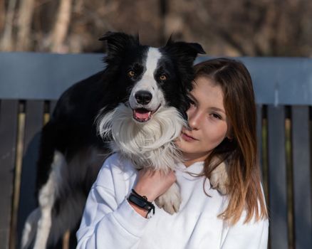 Caucasian woman hugging her dog Border Collie while sitting on a bench in autumn park