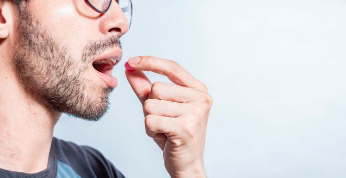 Man putting a pill in his mouth isolated. Close-up of a man taking an aspirin. Person taking a pill isolated, Close up of young man putting a pill in his mouth. Self-medication concept
