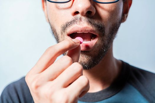 Person taking a pill isolated, Close up of young man putting a pill in his mouth. Self-medication concept, Man putting a pill in his mouth isolated, Close-up of a man taking an aspirin