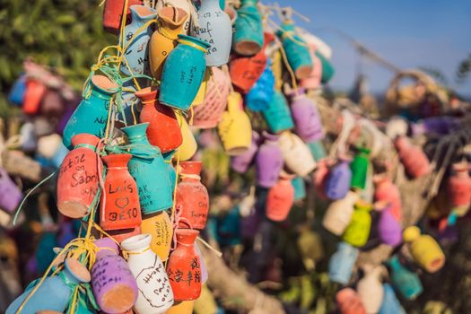 Wish tree. Small multi-colored jugs with inscriptions, wishes hanging on the branches of a tree., against the backdrop of sand ruins and blue sky.