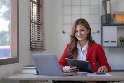 Asian Business woman using calculator and laptop for doing math finance on an office desk, tax, report, accounting, statistics, and analytical research concept..