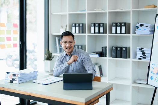 Portrait of a man business owner showing a happy smiling face as he has successfully invested her business using computers and financial budget documents at work.