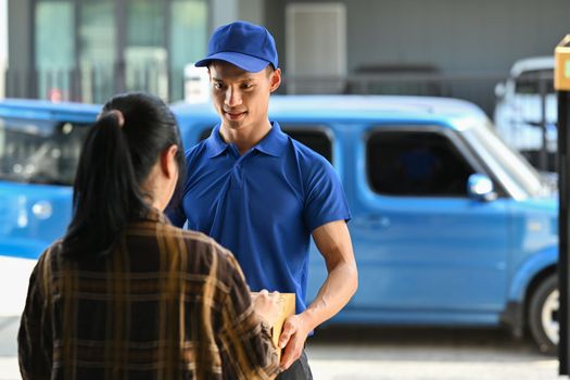 Friendly delivery man giving a cardboard box to woman customer at home. Delivery service, delivery home and shipping concept.