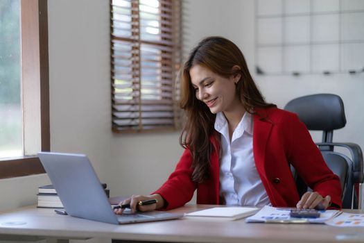 Asian Business woman using calculator and laptop for doing math finance on an office desk, tax, report, accounting, statistics, and analytical research concept..