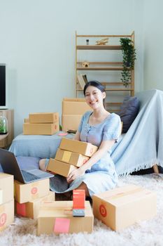 Starting small business entrepreneur of independent Asian woman smiling using computer laptop with cheerful success of online marketing package box items and SME delivery concept.