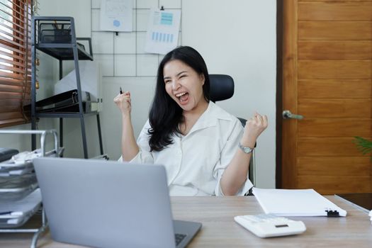 Portrait of a woman business owner showing a happy smiling face as he has successfully invested her business using computers and financial budget documents at work.