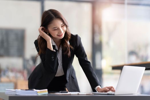 Focused young businesswoman standing at table in office, using laptop, looking at computer screen, reading or writing business email, searching information in internet, working on project..