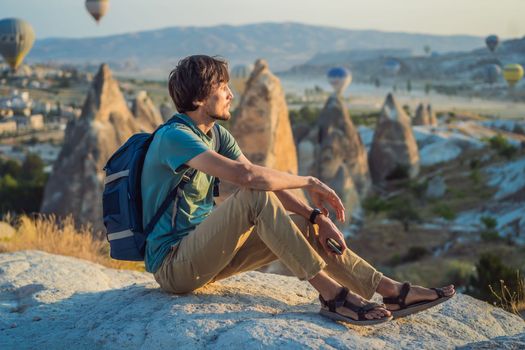 Tourist man looking at hot air balloons in Cappadocia, Turkey. Happy Travel in Turkey concept. Man on a mountain top enjoying wonderful view.