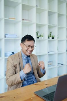 Portrait of an Asian male business owner standing with a computer showing happiness after a successful investment.