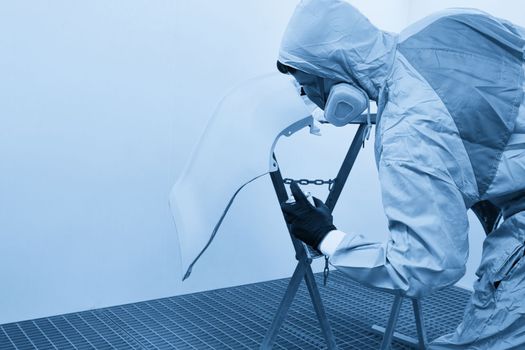 Mechanic painting bumper of a car with sprayer in painting booth