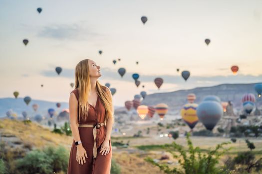 Tourist woman looking at hot air balloons in Cappadocia, Turkey. Happy Travel in Turkey concept. Woman on a mountain top enjoying wonderful view.