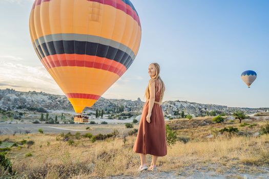 Tourist woman looking at hot air balloons in Cappadocia, Turkey. Happy Travel in Turkey concept. Woman on a mountain top enjoying wonderful view.