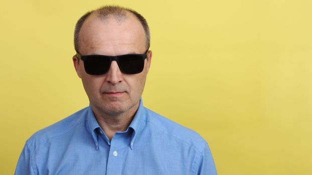 A man in black sunglasses on a yellow background.