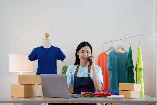 Beautiful asian woman online seller confirming orders from customer on the phone, Start small businesses SME owners female entrepreneurs use a laptop at home,pack and delivery situation concept..