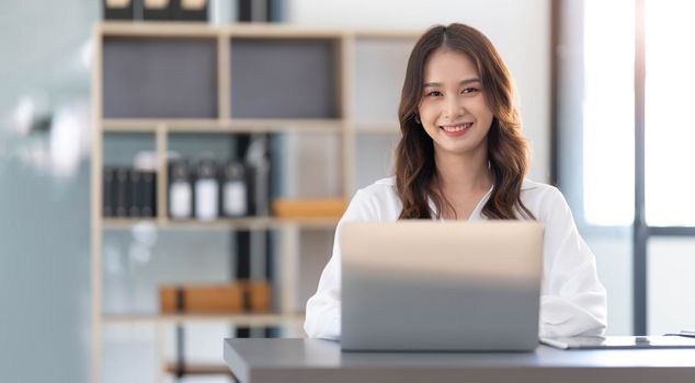 Charming Asian woman working at the office using a laptop Looking at the camera...