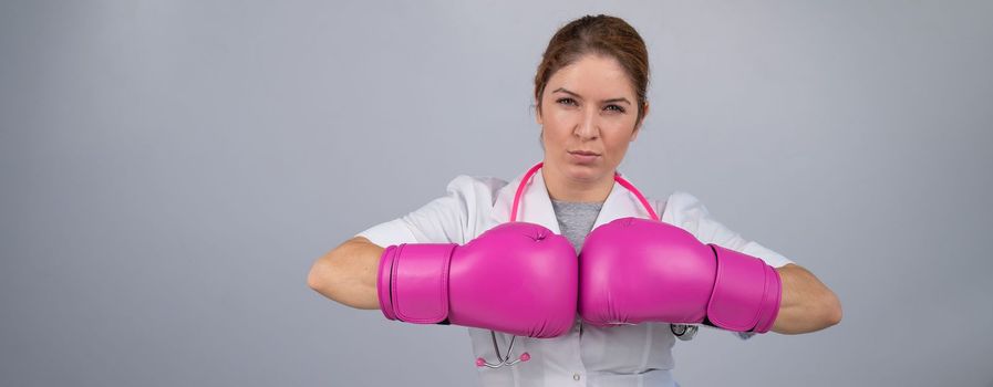 Female doctor in pink boxing gloves with a pink ribbon on a gray background. Fight against breast cancer. Widescreen