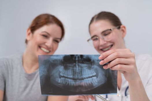 A woman doctor and a patient at the reception are discussing an x-ray of the jaw