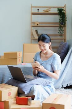 Starting small business entrepreneur of independent young Asian woman online seller is using computer and taking orders to pack products for delivery to customers. SME delivery concept.