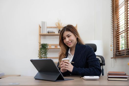 Asian woman Using laptop computer and working at office with calculator document on desk, doing planning analyzing the financial report, business plan investment