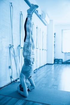 Handsome woman having yoga practice and standing on head in white lit room. Concept of physical and mental health, happy living and well being.