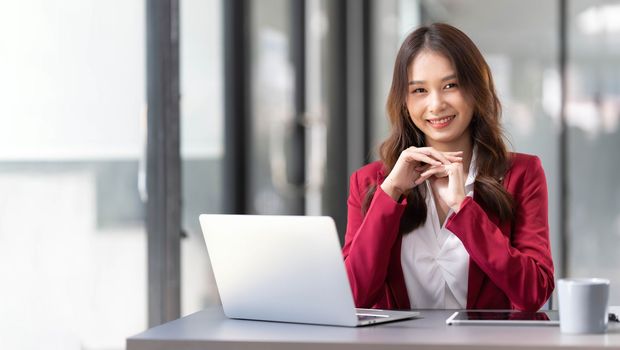 Portrait of smiling beautiful business asian woman in pink suit working in home office desk using computer. Business people employee freelance online marketing e-commerce, work from home concept..
