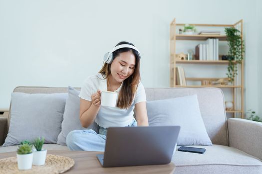 asian teenage girl using computer and wearing headphones at sofa.