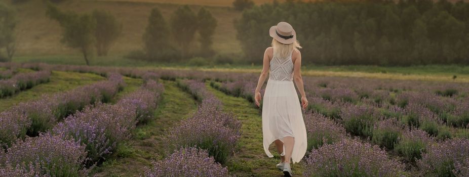 Beautiful young woman in wicker hat and white dress in a lavender field with.