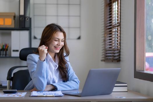 Portrait of an excited young asian girl using laptop computer and celebrating success for online...