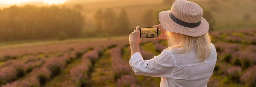 Young blond woman traveller wearing straw hat in lavender field surrounded with lavender flowers